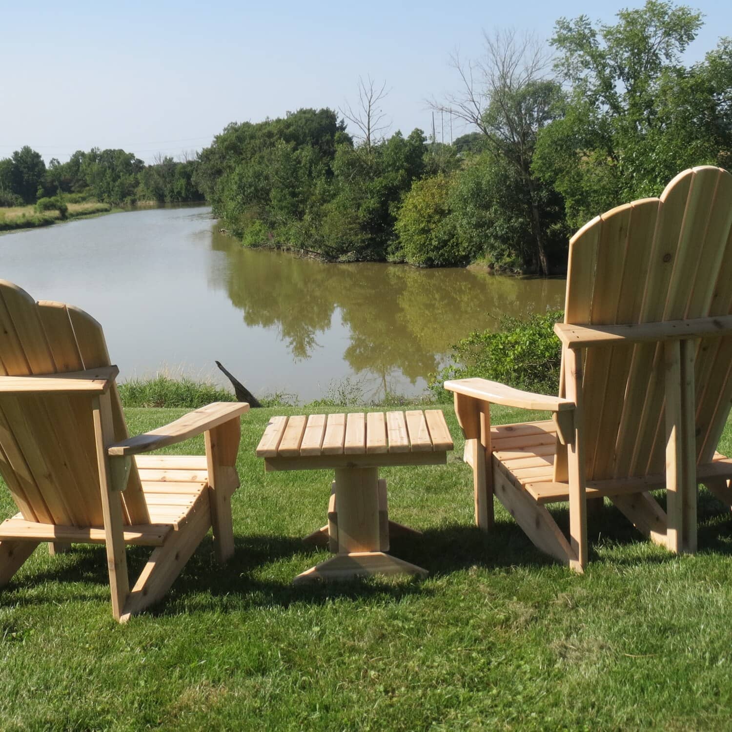 Pair of cedar Muskoka chairs and a pedestal side table on a lawn beside a pond